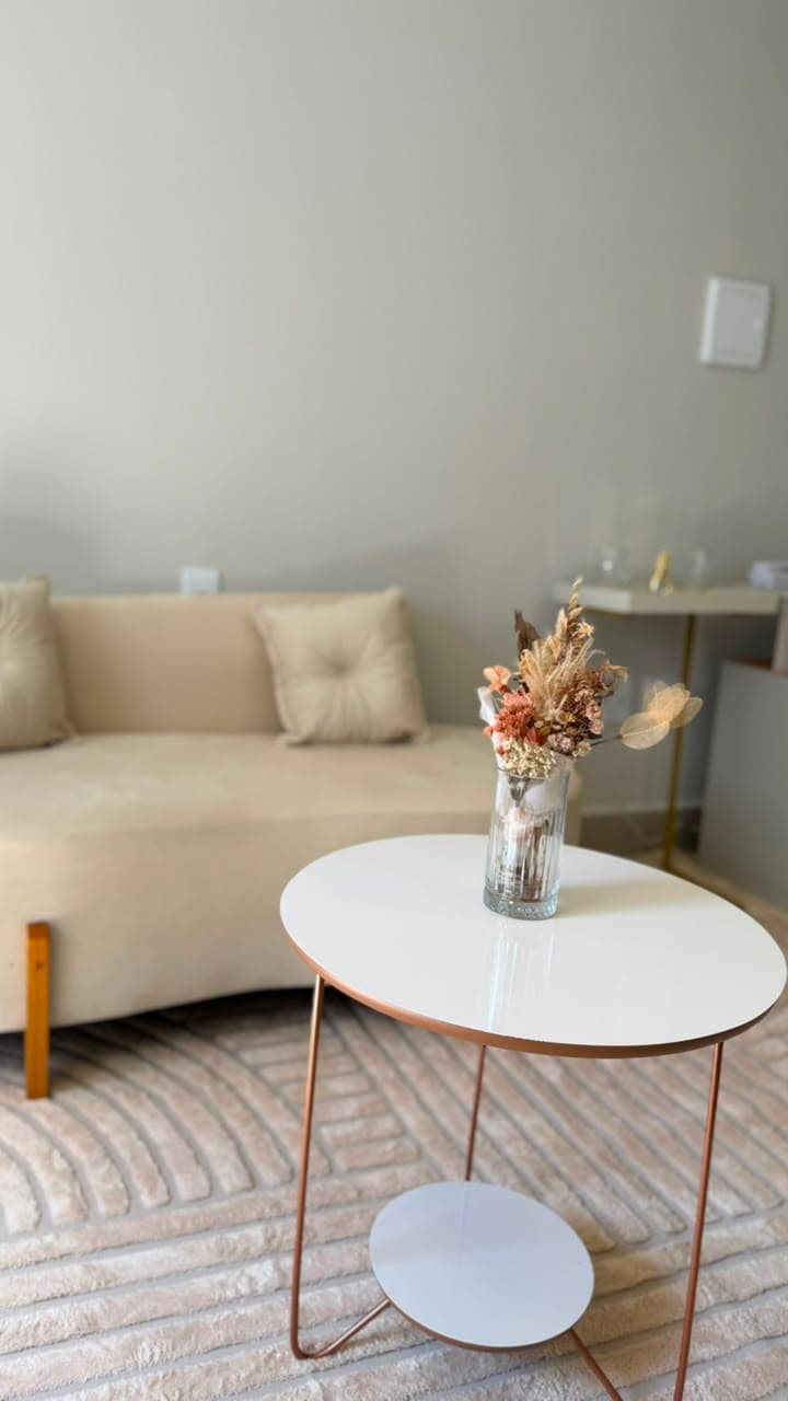 Sala de atendimento com sofá, poltronas, mesa de trabalho e mesa de centro com arranjo de flores secas